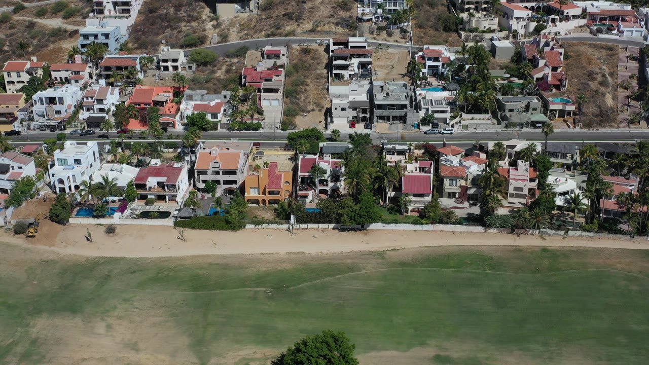 Aerial view of coastal homes beside a sandy beach and shallow water.