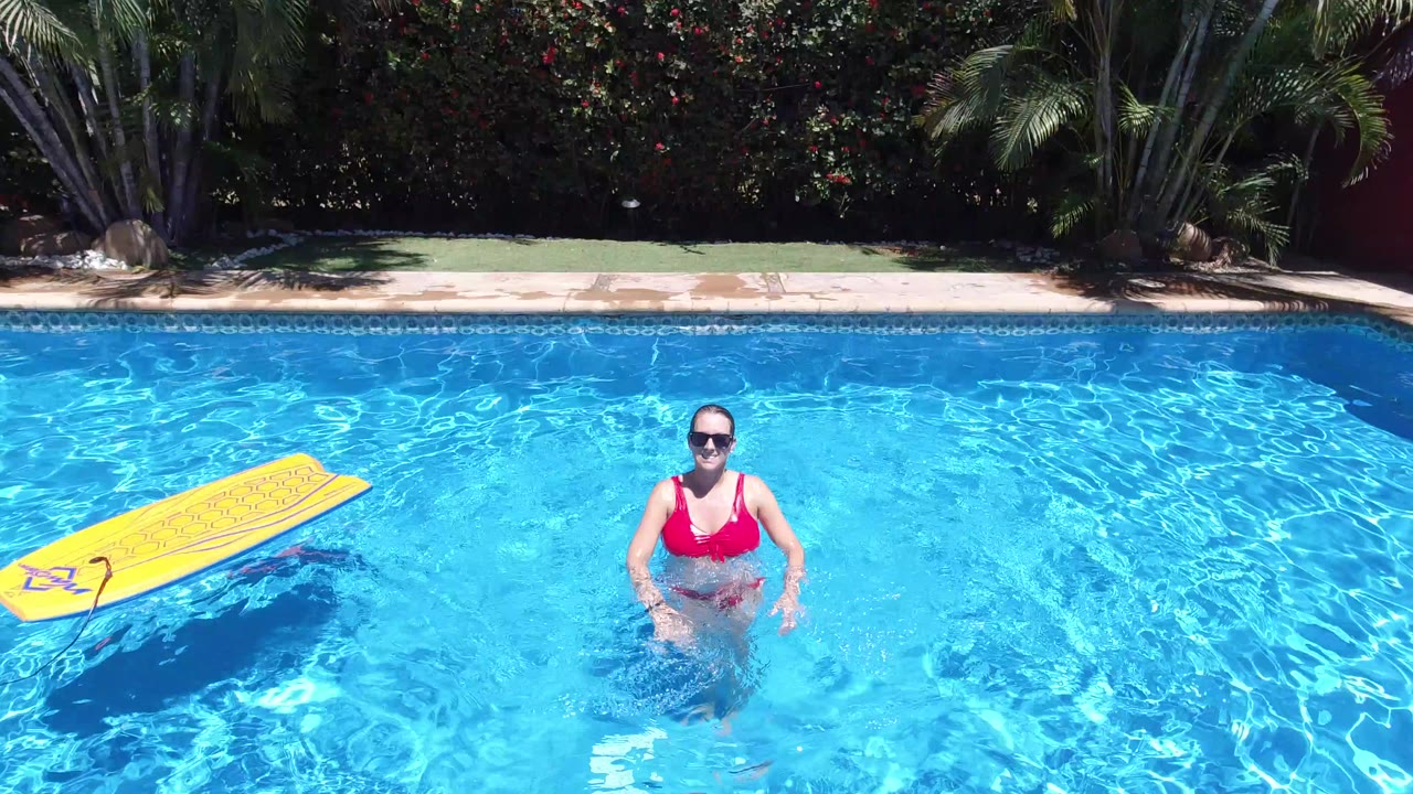 Woman in red bikini standing in blue swimming pool beside a yellow float.