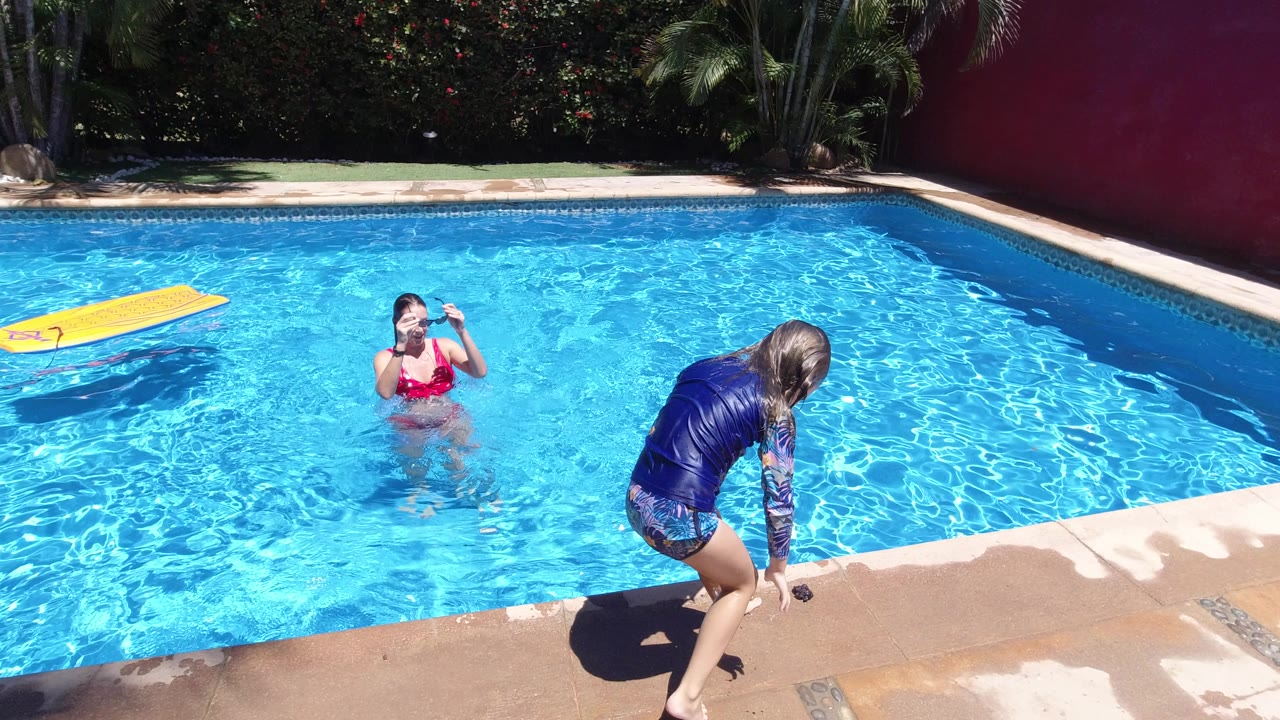 In Los Cabos, Mexico, the girl bends near the edge of the pool with one hand close to the deck as the woman in the water watches from the center-left of frame.