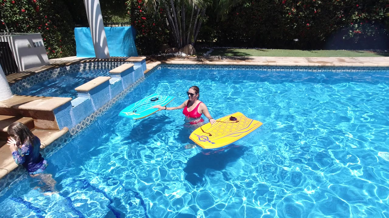 Woman and child in a swimming pool with two bodyboards.