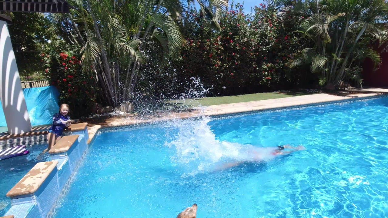 Person splashing into a blue pool while a child sits near the edge.