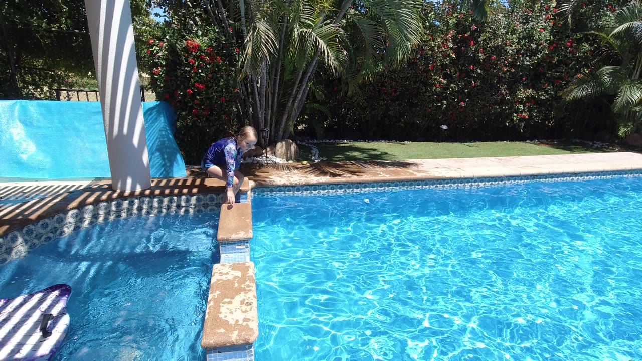 Blonde child crouching near a poolside diving board.