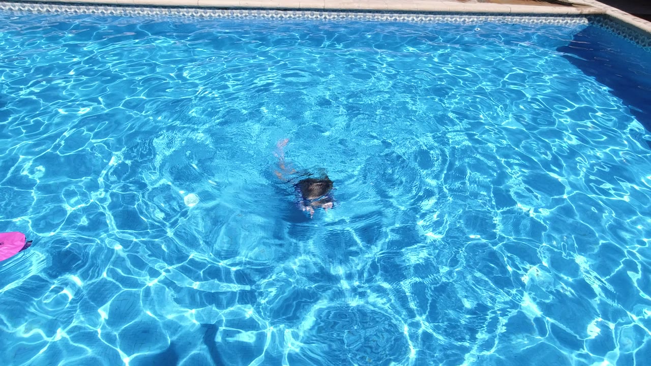 The child remains mostly underwater in the center of the Los Cabos pool, with bright caustic light patterns and the pool coping visible along the top edge.