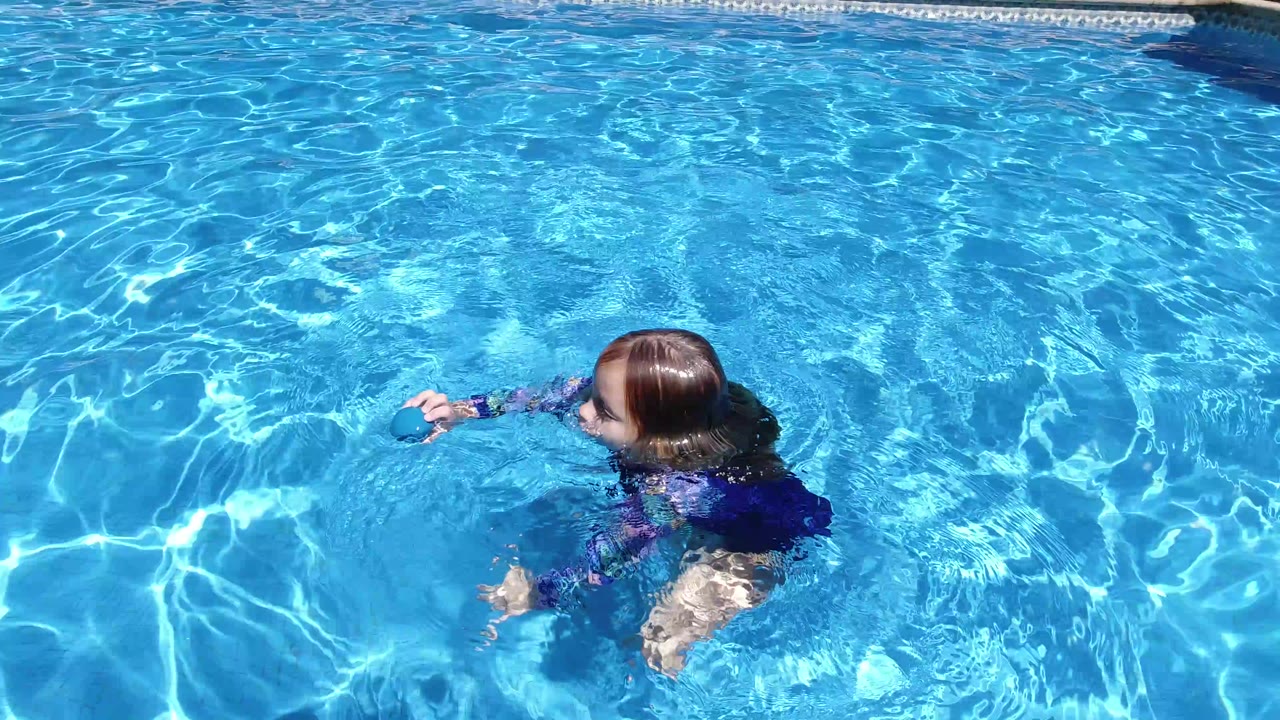 Child swimming in a bright blue pool near a small floating ball.