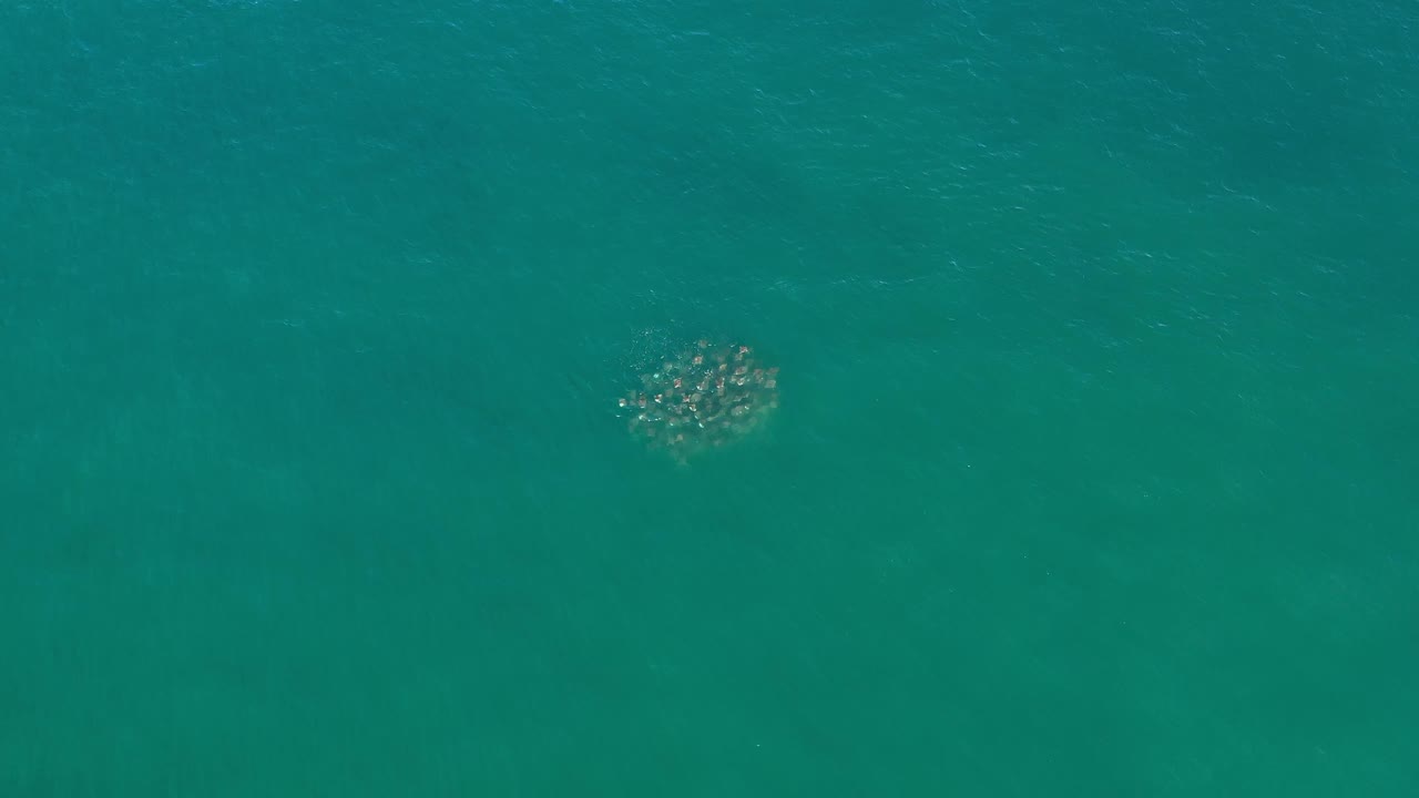 A small unidentified marine cluster sits below the surface of teal Los Cabos water, slightly right of center, with no shoreline and no visible people.