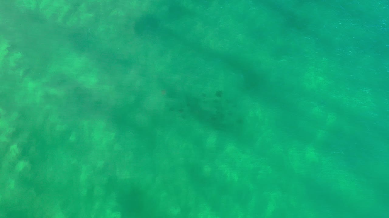 Overhead view of turquoise seawater in Los Cabos, Mexico, with darker underwater patches near the upper frame and no visible people.
