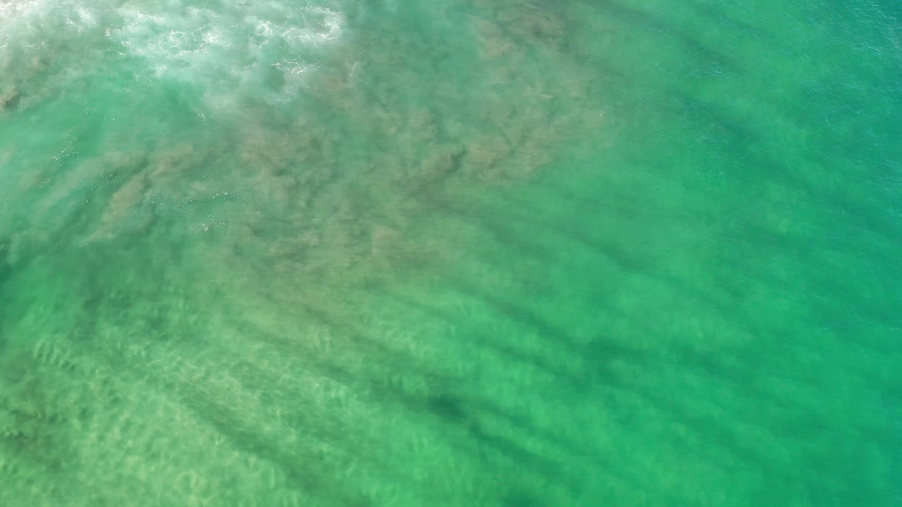 Overhead view of green-tinted water in Los Cabos, Mexico, with cloudy sediment near the upper left and no visible people.
