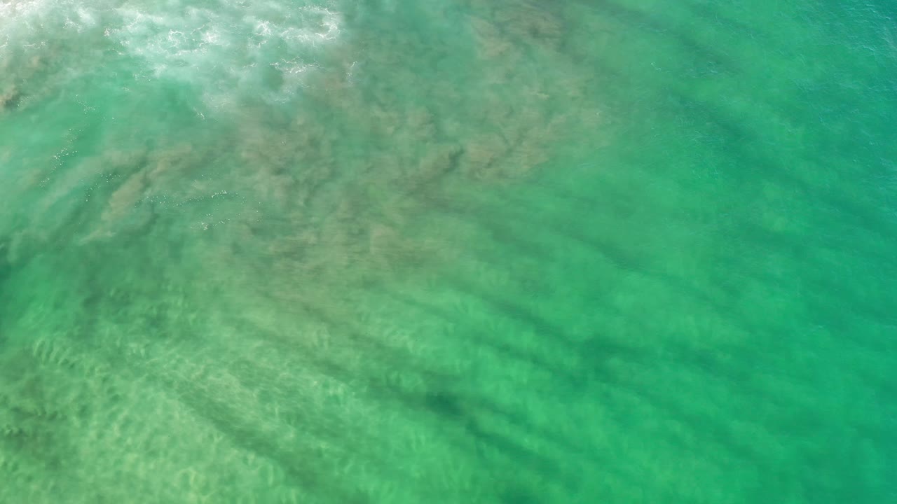 Overhead Los Cabos water view with turquoise color, pale sediment haze spreading across the left side, and no visible people.