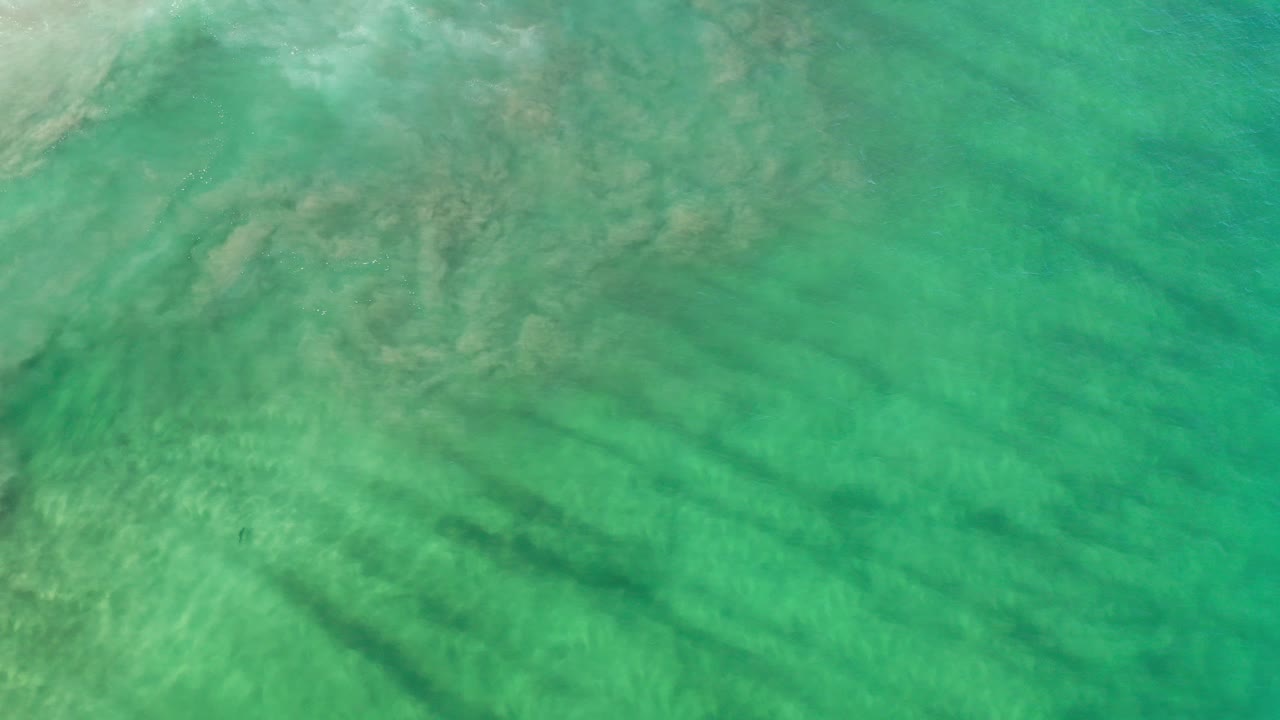 Clear green water in Los Cabos with pale sandy areas and dark submerged shadow lines near the lower half, no visible people.
