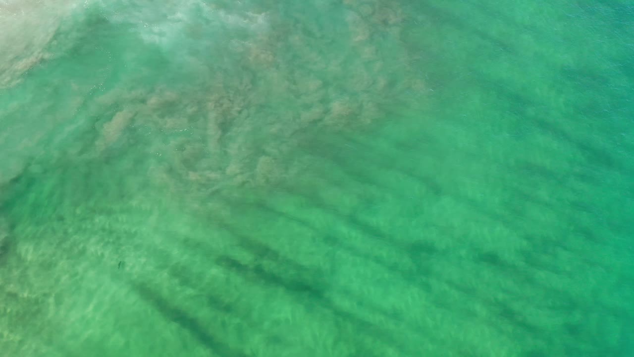 Los Cabos water fills the frame with soft ripples, muted sandy patches, and a darker diagonal shadow area across the lower left, no visible people.