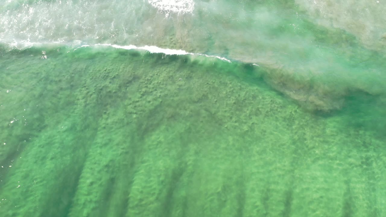Top-down Los Cabos shoreline water with a brighter white breaker near the upper frame and darker underwater streaks below, no visible people.