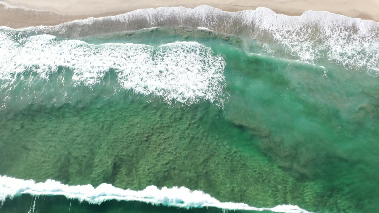 Overhead teal surf breaking onto pale sand.