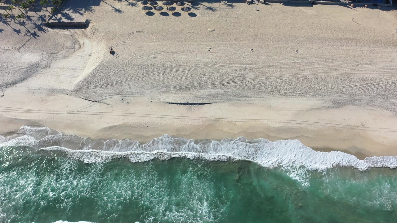 Surf and sand viewed from directly above near beach structures.