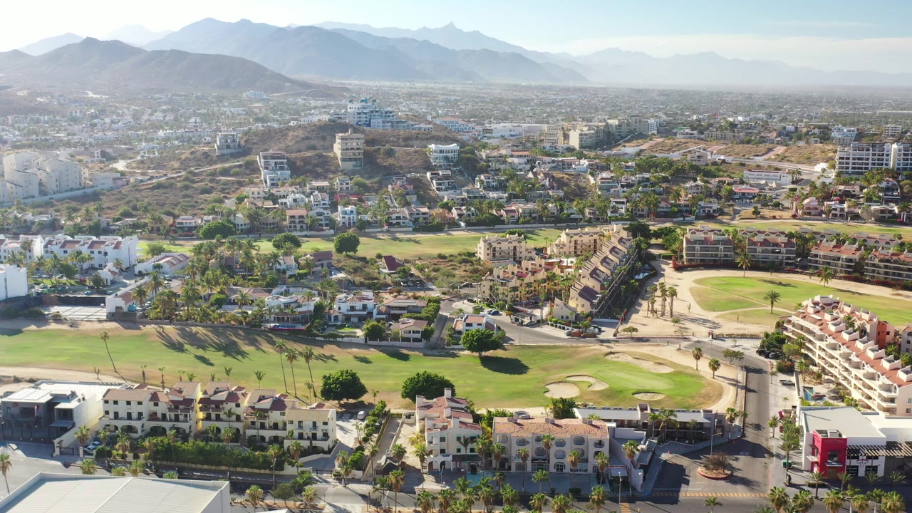 Aerial view of residential buildings, golf greens, roads, and mountains.
