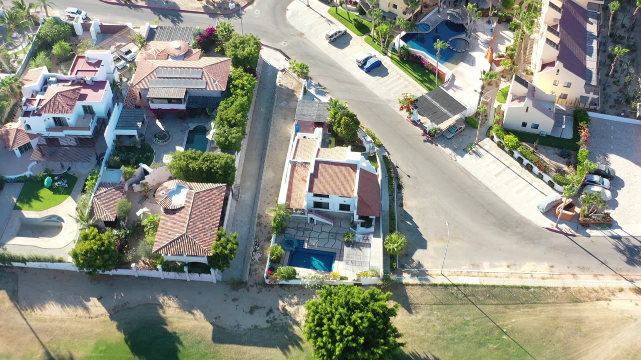 Overhead view of sunlit homes, pools, streets, and landscaping.