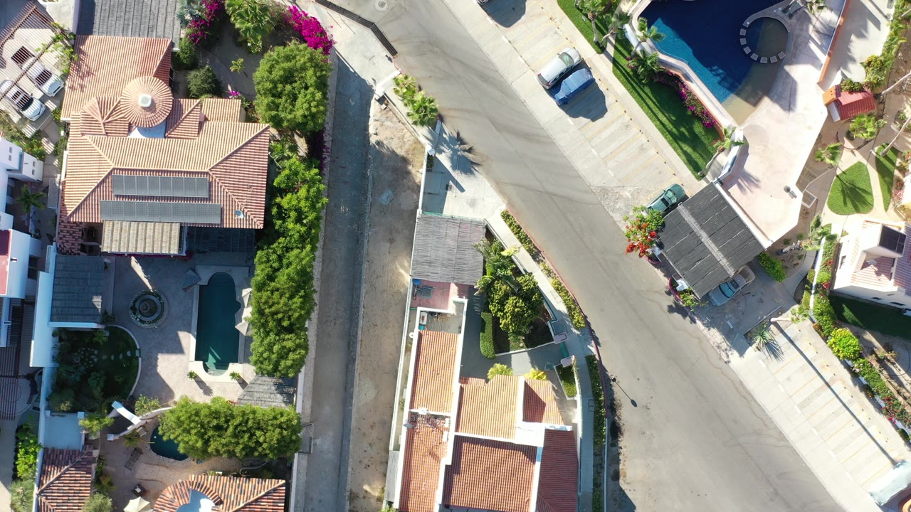 Aerial view of houses, a paved intersection, yards, and a small pool.
