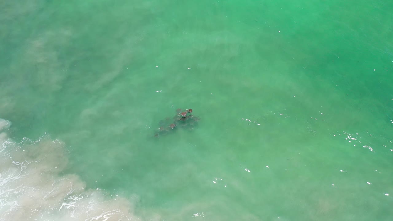 Turquoise water with a small dark submerged area and thin white surf at the edge.