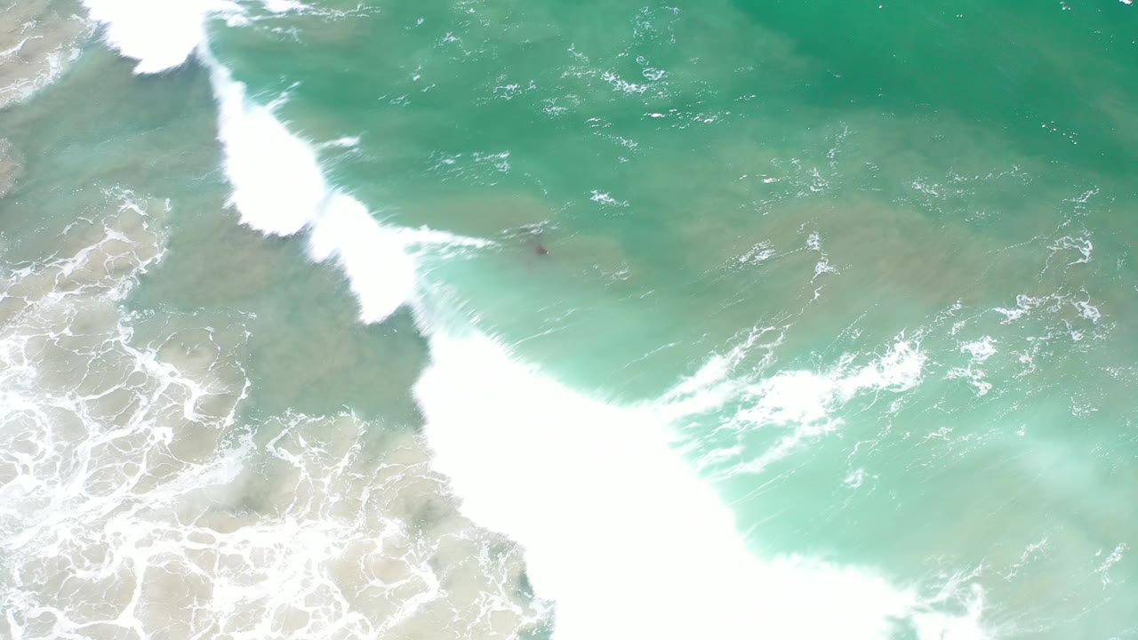 Large white wave breaking across clear green-blue water.