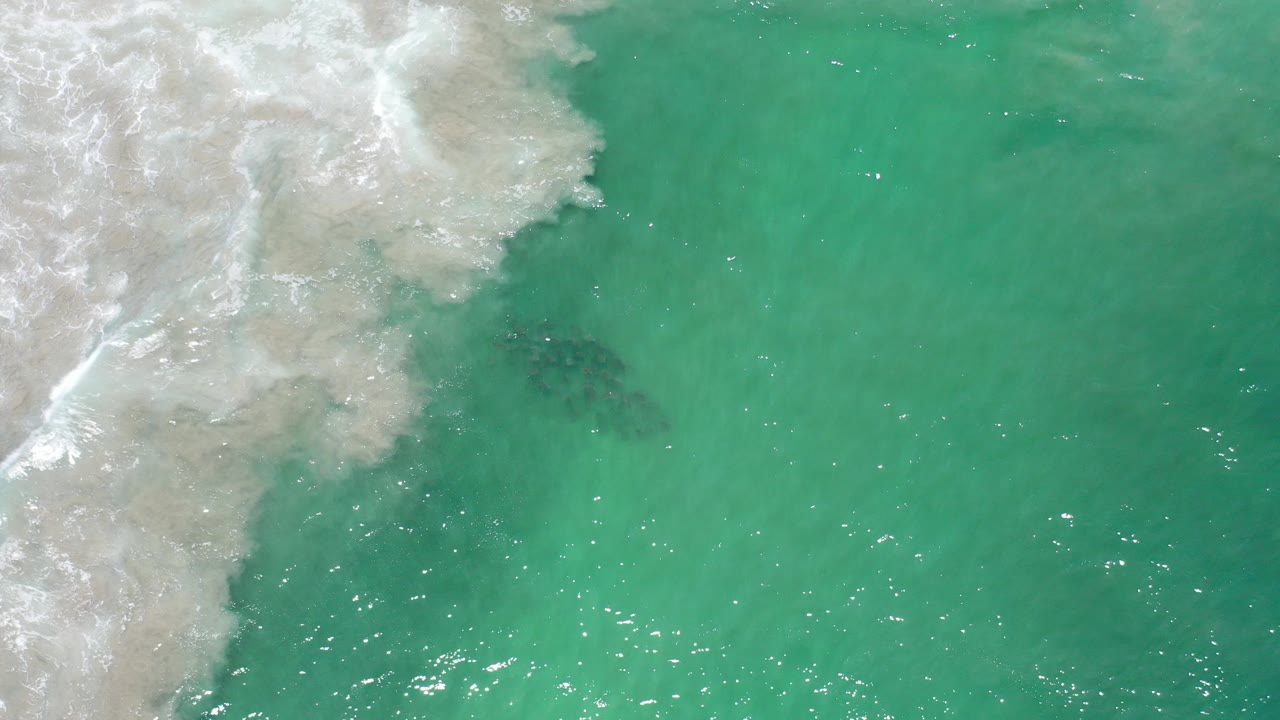 Overhead view of turquoise seawater in Los Cabos, Mexico, with white surf spreading from the upper left and no visible people.