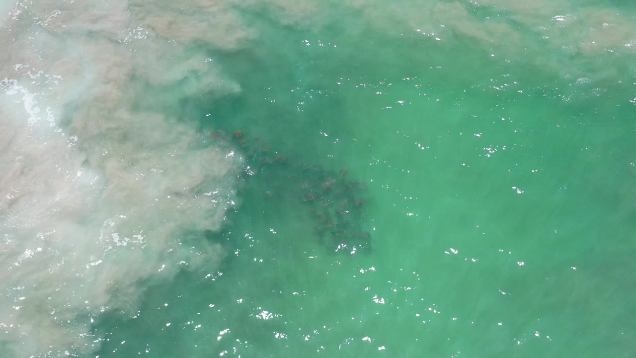 Overhead view of turquoise ocean water in Los Cabos, Mexico, with white foam drifting in from the left and no visible people.