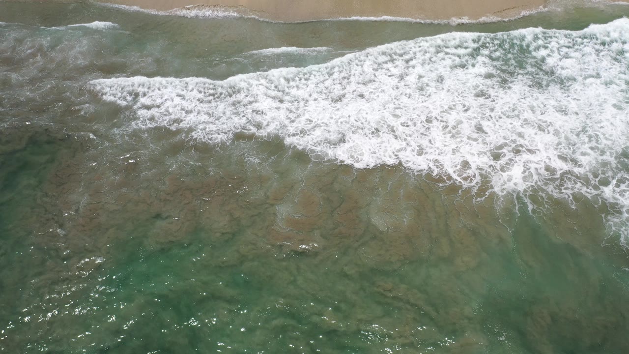 Overhead surf washing toward a sandy beach.