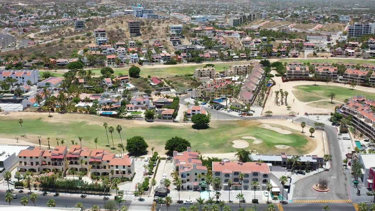 Aerial view of golf course greens, villas, streets, and hillside housing.