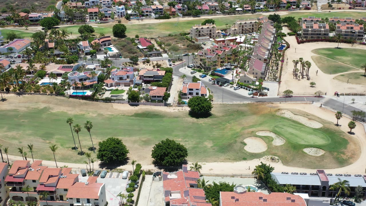 High view of golf-course grass, sand traps, homes, and parked cars.