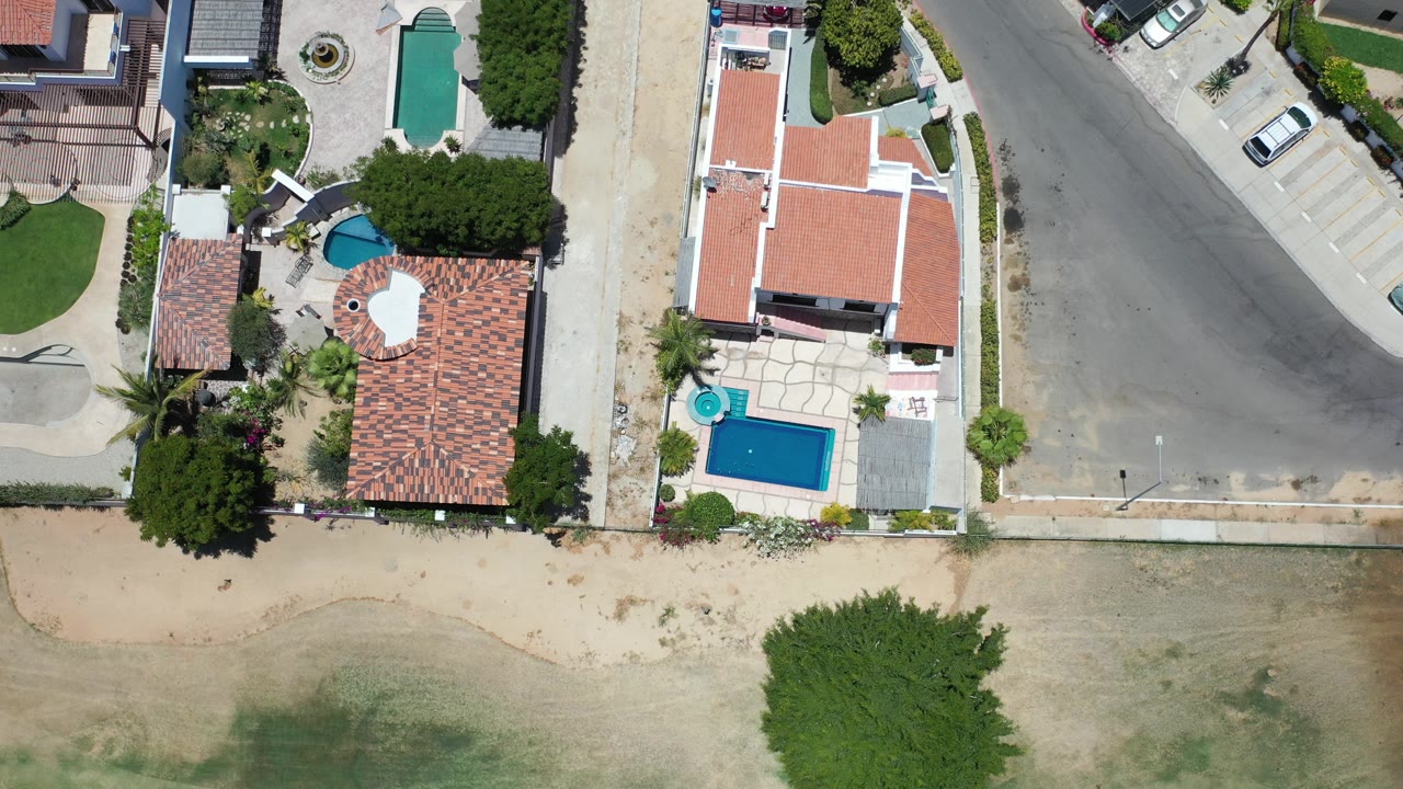 Overhead view of houses, pools, road, and sandy lots.