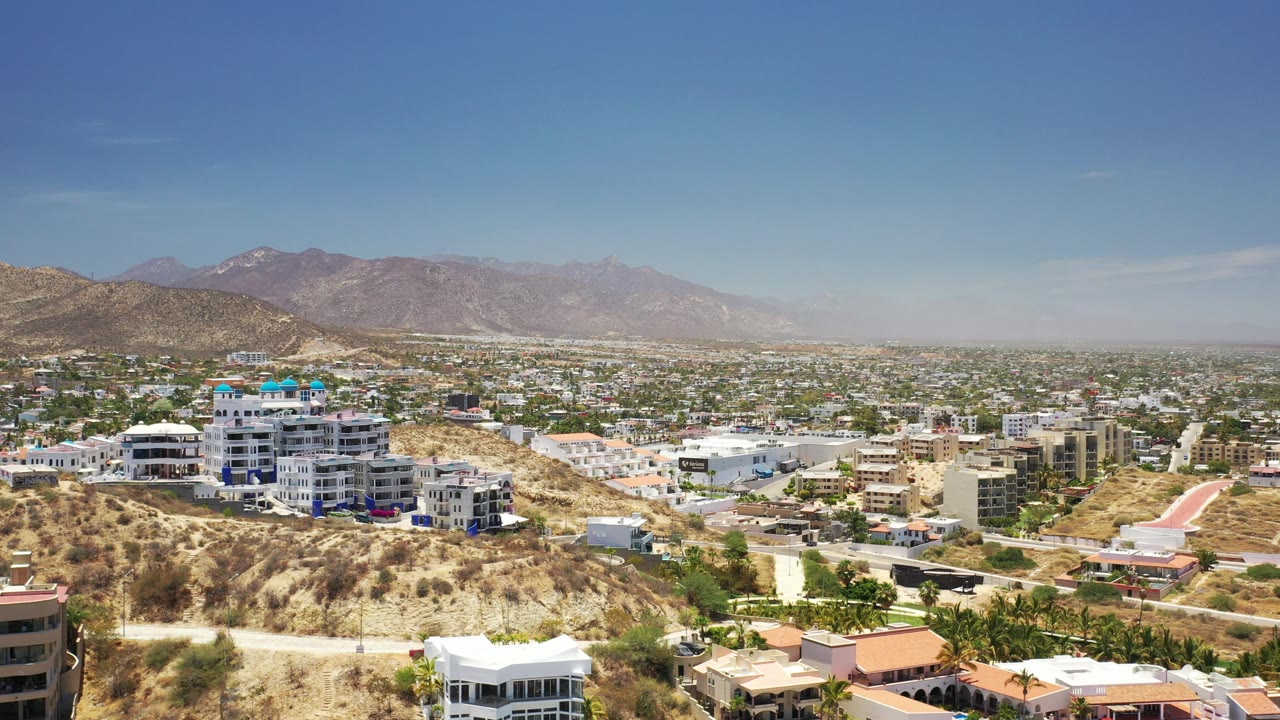 Sunlit town and dry hills with buildings, roads, and mountains beyond.