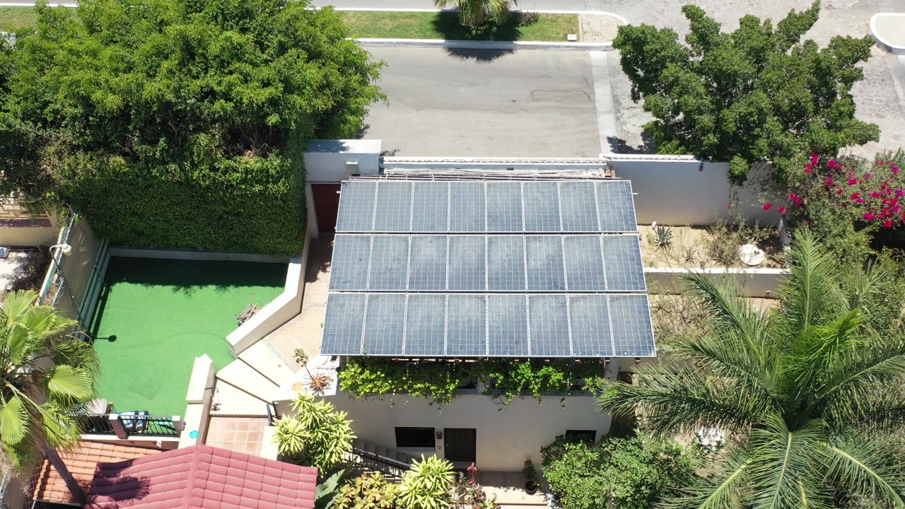 Overhead view of a house roof, green pool area, palms, hedges, and street.