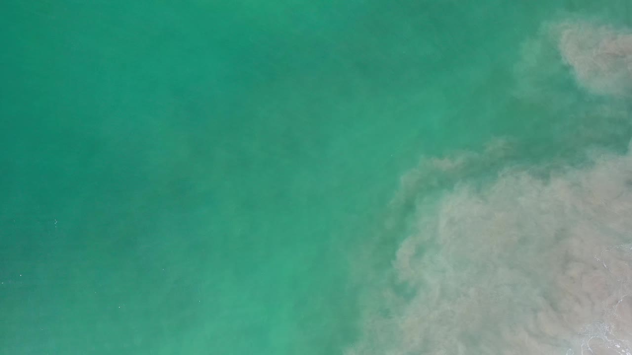 Overhead Los Cabos water view with turquoise green water dominating the frame and cloudy brown sediment along the right edge, with no visible people.