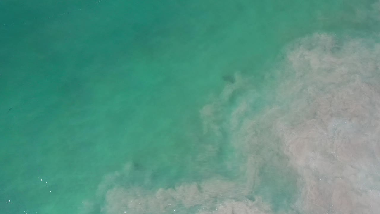 Aerial view over Los Cabos turquoise water with the pale underwater plume shifted slightly farther across the right side and no visible people.