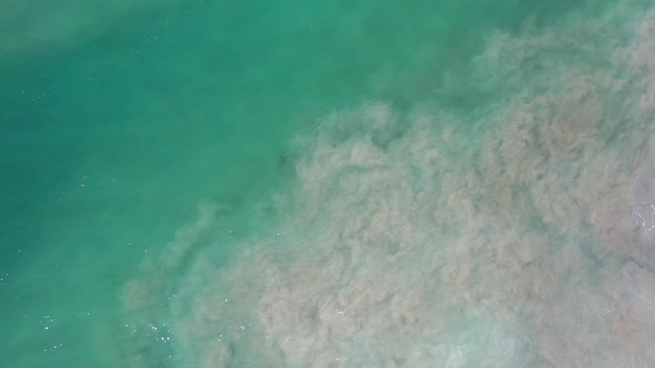 Sand cloud beneath teal water