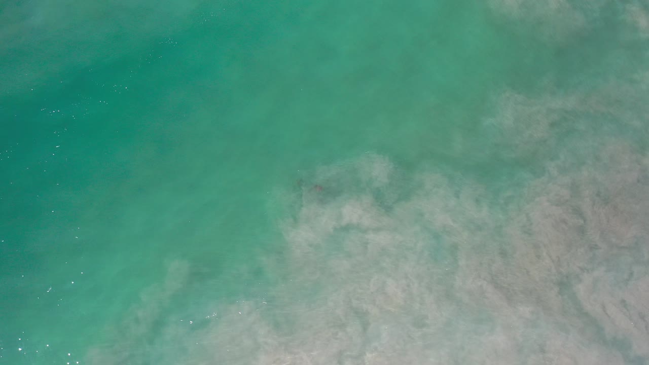 Overhead view of turquoise Los Cabos ocean water with pale underwater clouding across the lower right and no visible people.