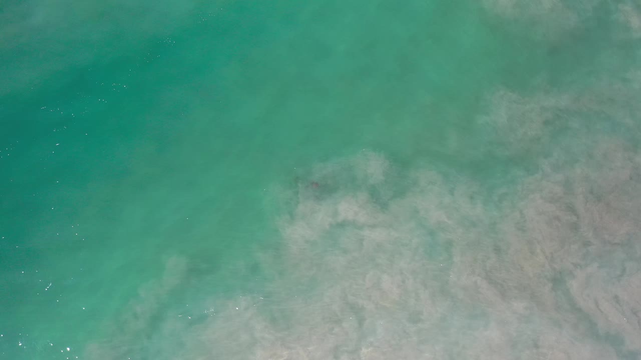 Aqua Los Cabos water fills the frame, with pale swirling texture spreading across the lower half and no visible people.