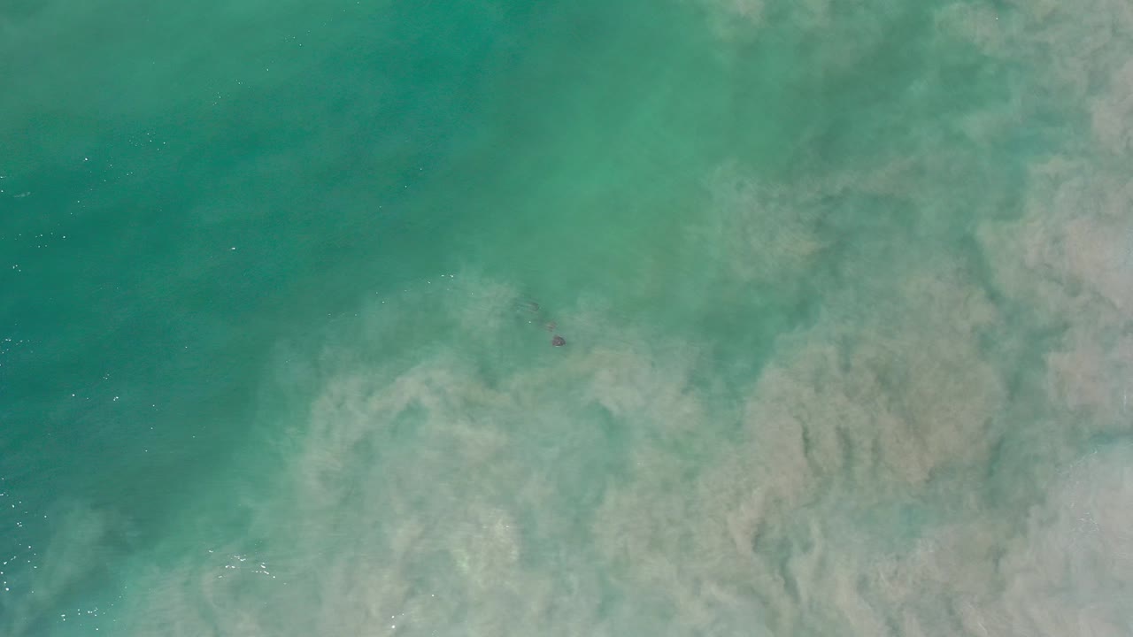Green ocean water and cloudy sand over submerged rocks
