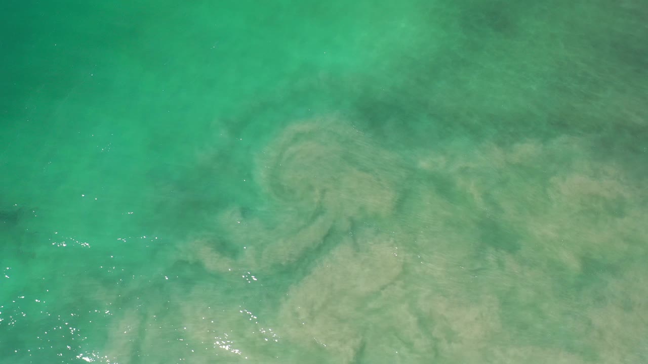 Turquoise-green seawater in Los Cabos fills the frame with cloudy tan sediment near the lower half and no visible people.