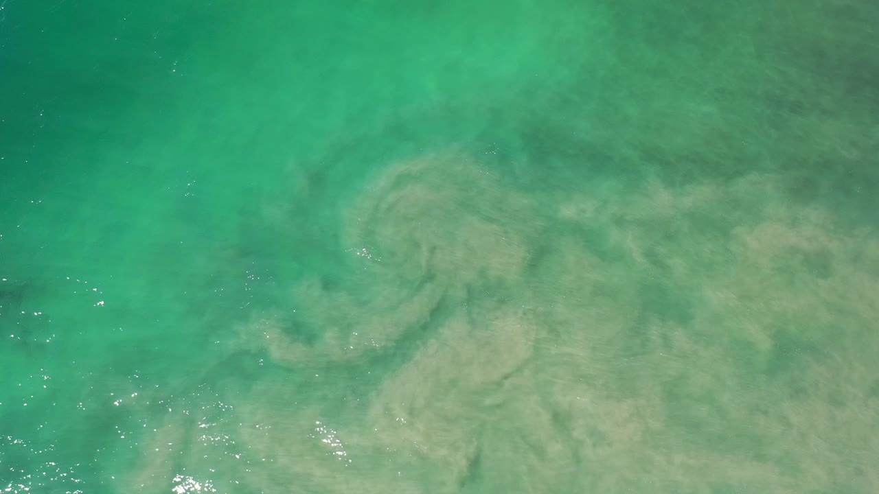 Aqua seawater with a spiral-like cloudy sediment pattern