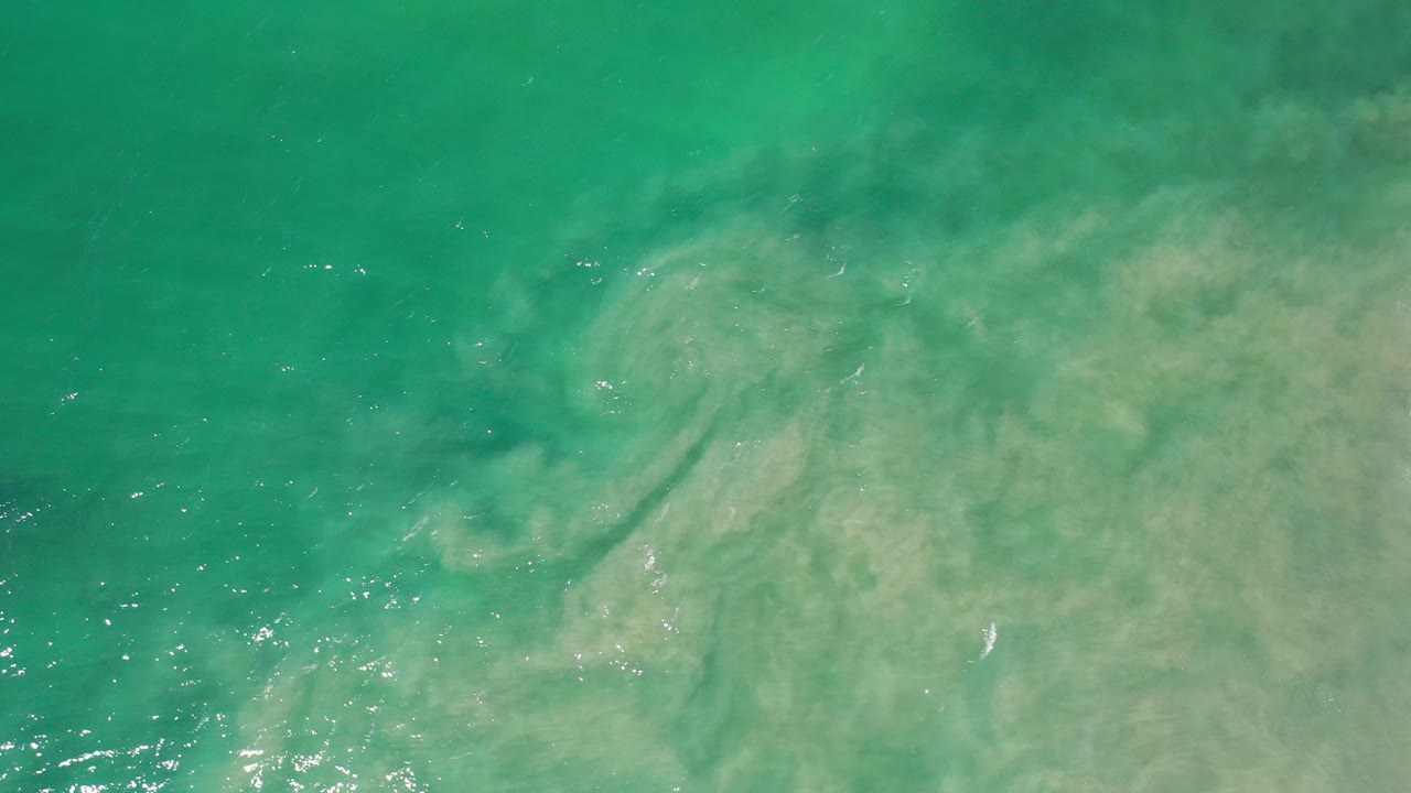 Overhead view of green seawater washing over pale circular sand patterns in Los Cabos, Mexico, with no visible people.