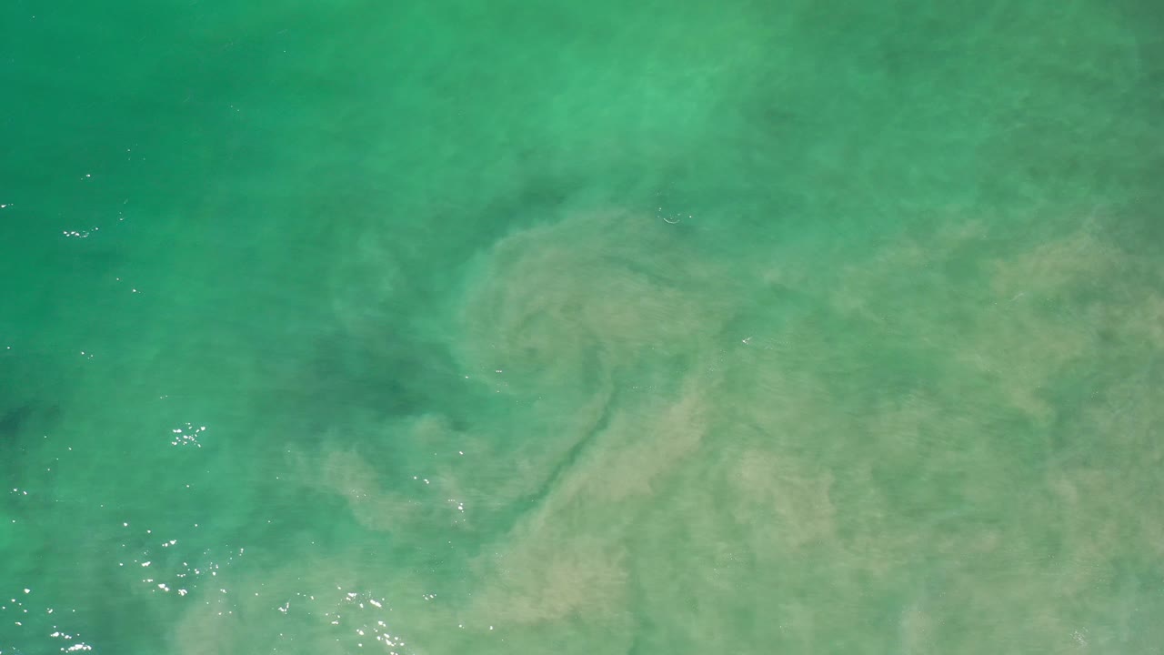 Brown dirt plume curling through turquoise coastal water