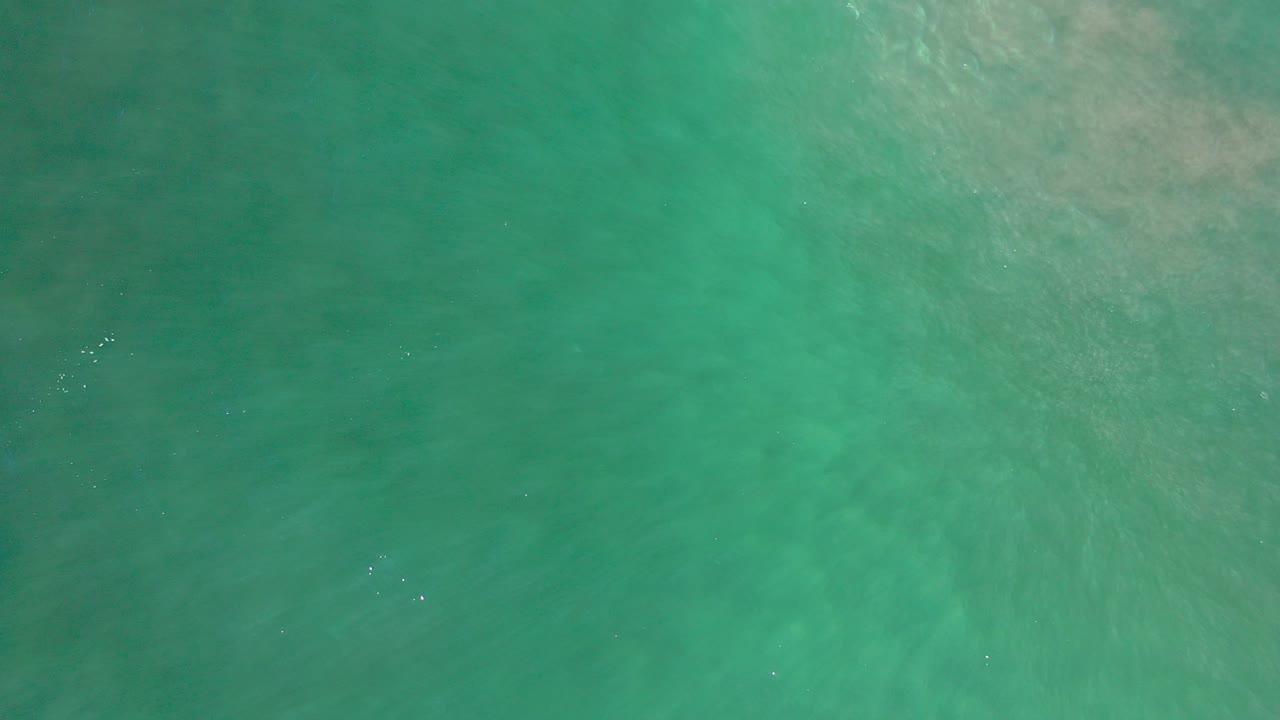 Overhead view of turquoise ocean water in Los Cabos, Mexico, with muted sandy clouding beneath the surface and no visible people.
