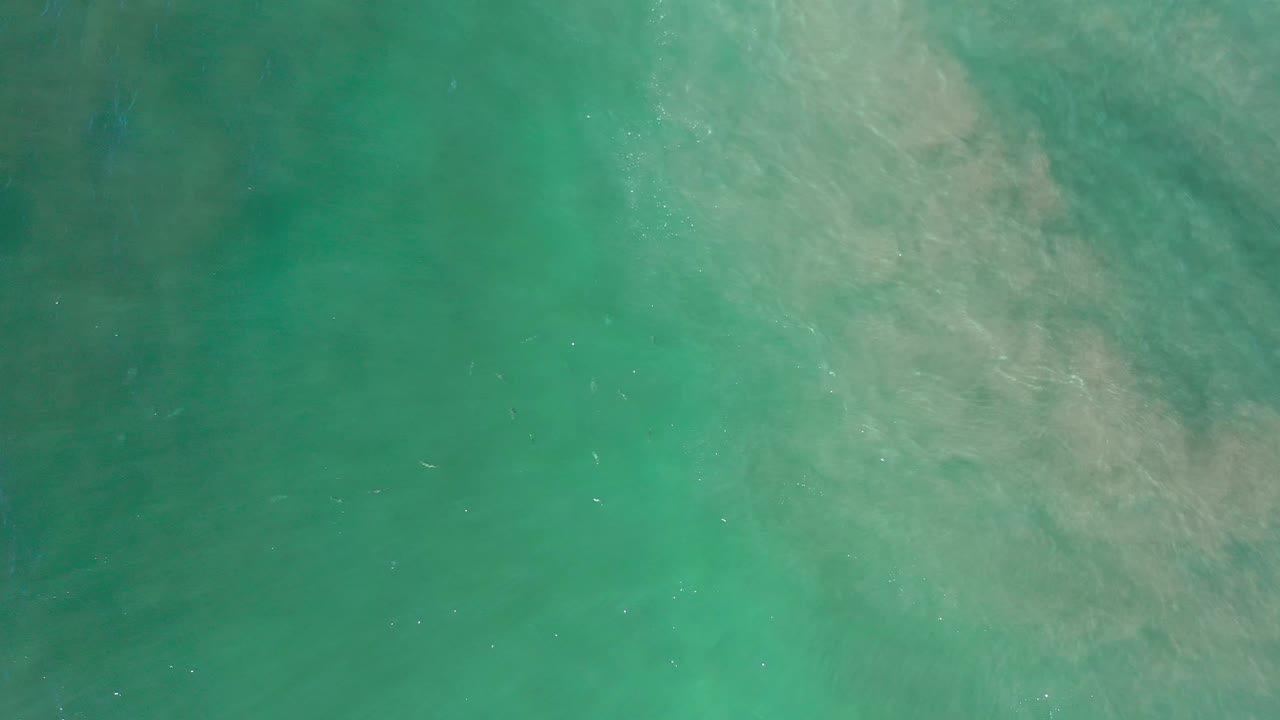 Teal water fills the frame in Los Cabos, with faint surface ripples and a diffuse pale patch drifting through the upper half, no visible people.