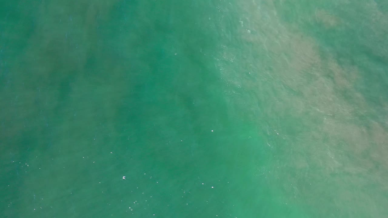Aerial Los Cabos ocean frame with green water, a broader pale patch across the upper right, scattered white flecks, and no visible people.