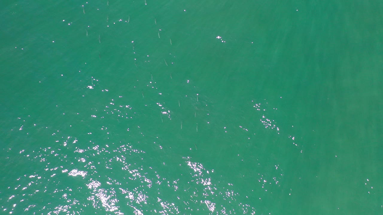 Top-down view of blue-green ocean water in Los Cabos, Mexico, with small ripples and bright sun glints near the lower left, no visible people.