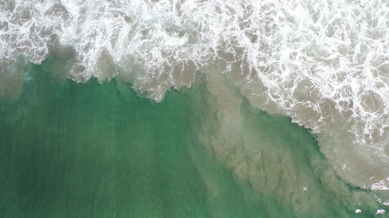 White surf line crossing green water over sand