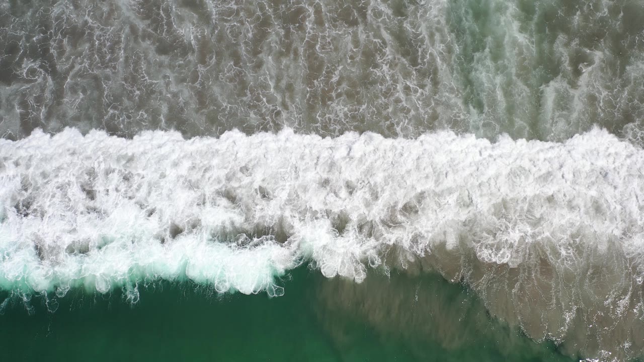 Breaking surf over green water from above