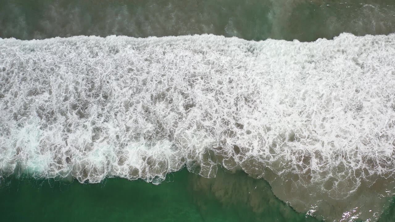 White breaking surf over green and tan beach water