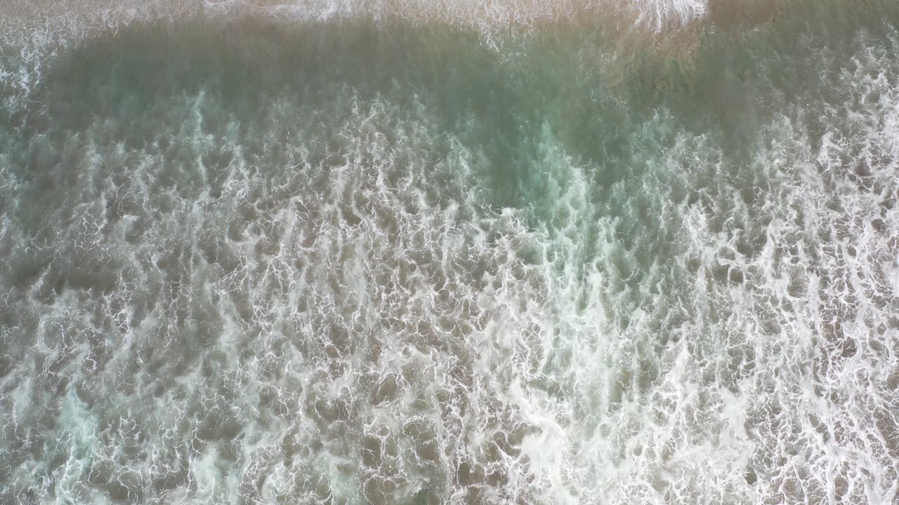 Foamy wave pattern seen from directly above a beach.