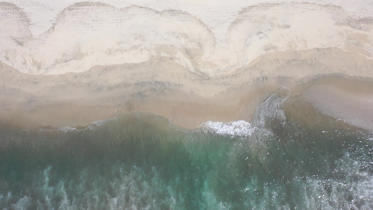 Overhead surf meeting pale sand
