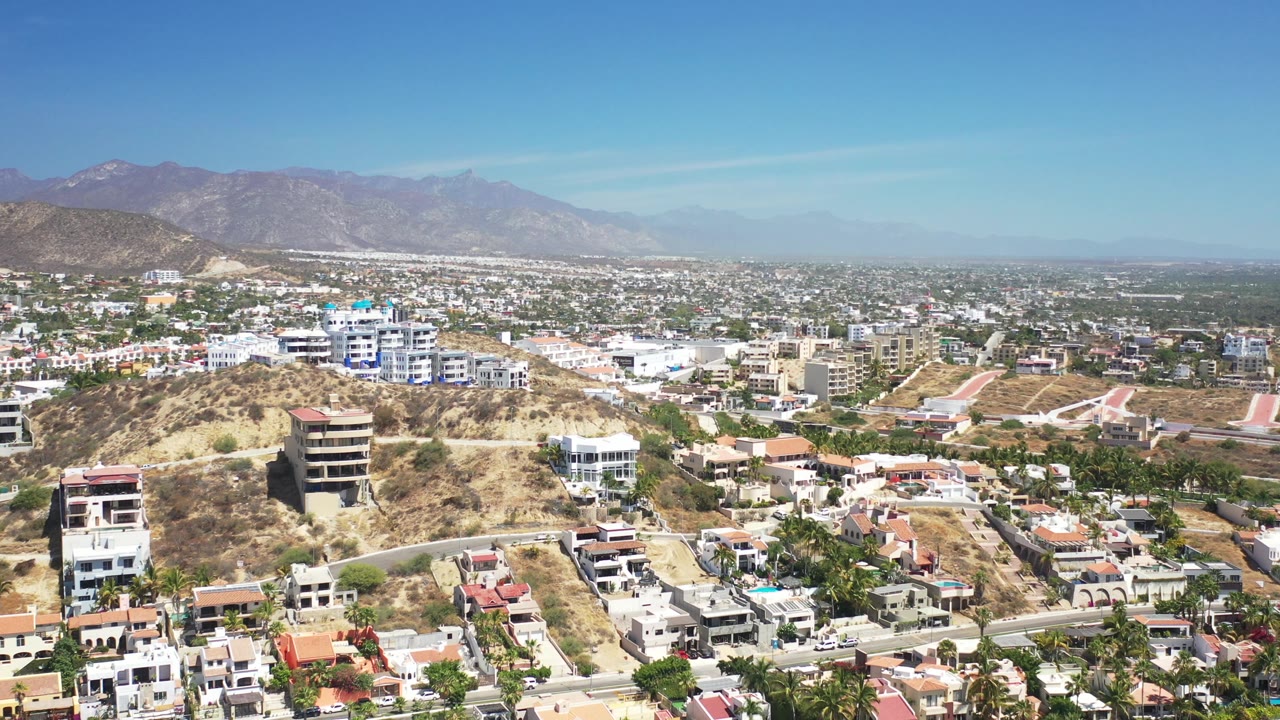 Aerial view of hillside homes, roads, town blocks, and distant mountains.
